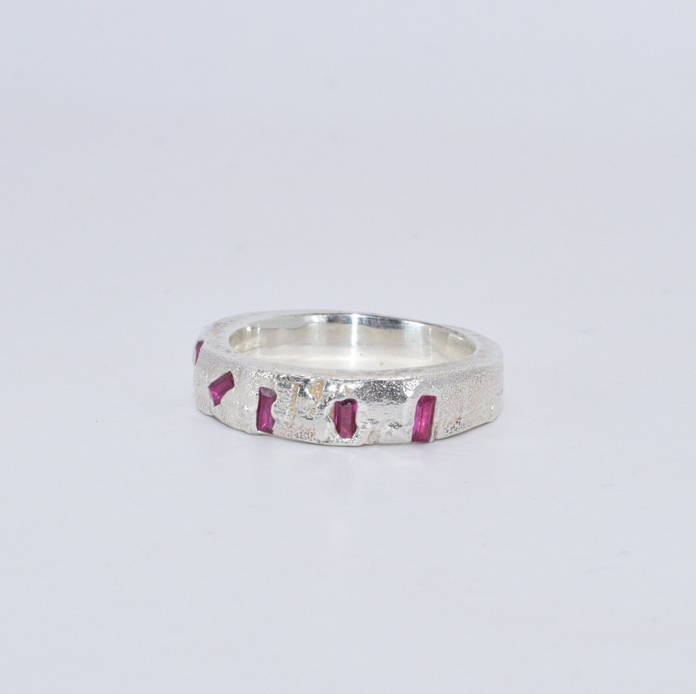 Silver ring with five ruby baguettes scattered across the front in an organic, asymmetrical formation