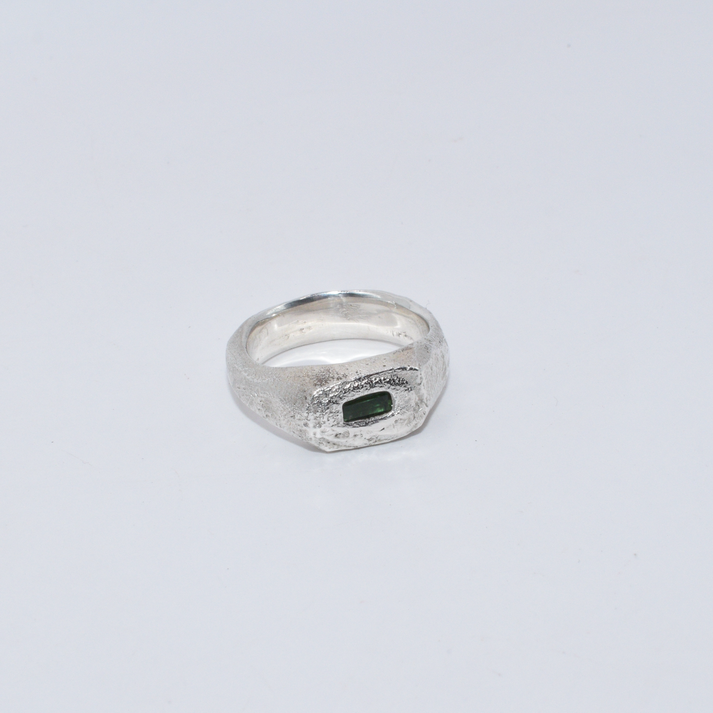 Silver ring with a green stone on a light gray background