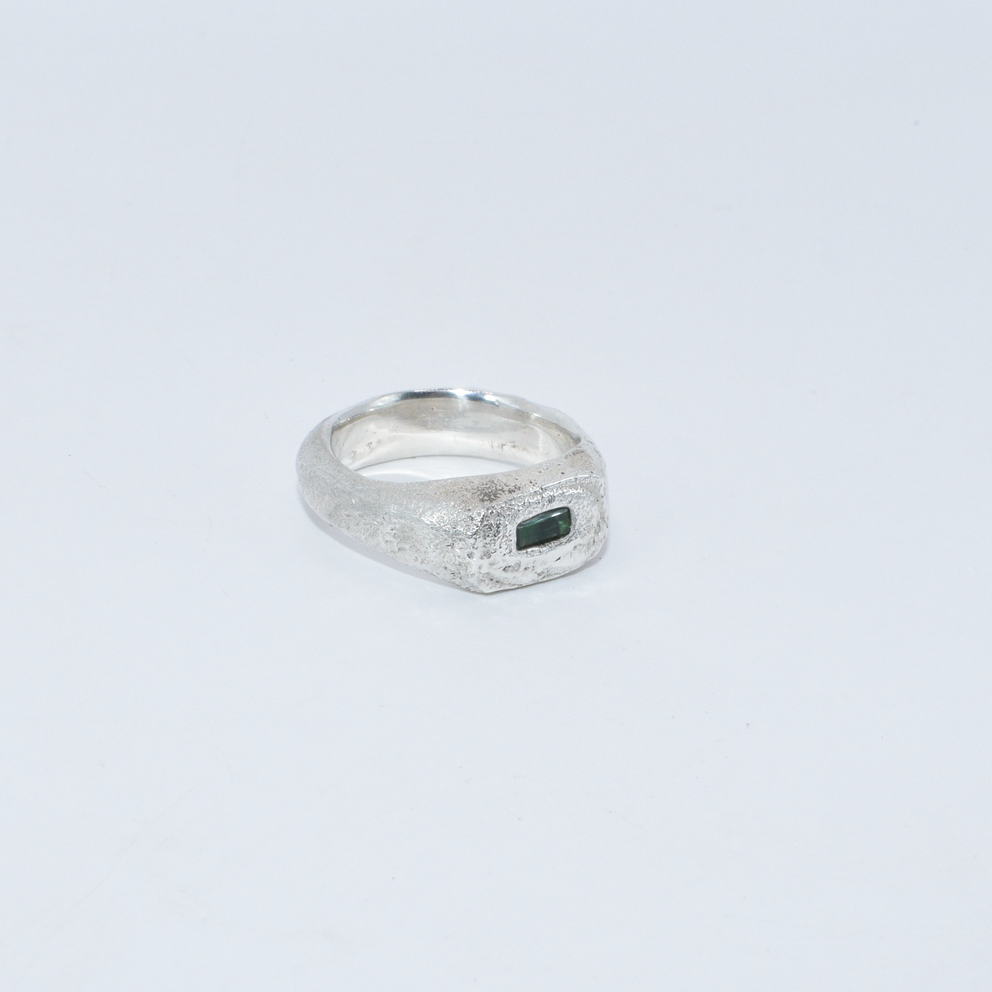 Silver ring with a green emerald stone on a light grey background