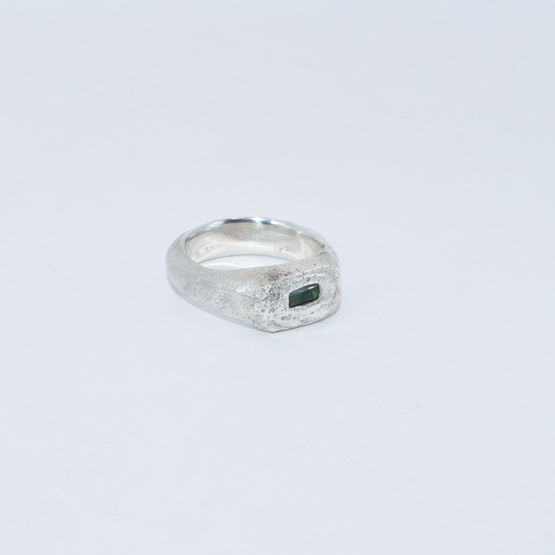 Silver ring with a green emerald stone on a light grey background