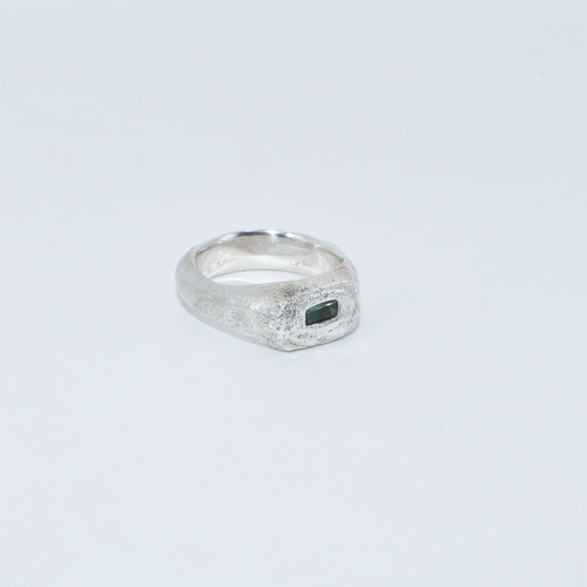 Silver ring with a green emerald stone on a light grey background
