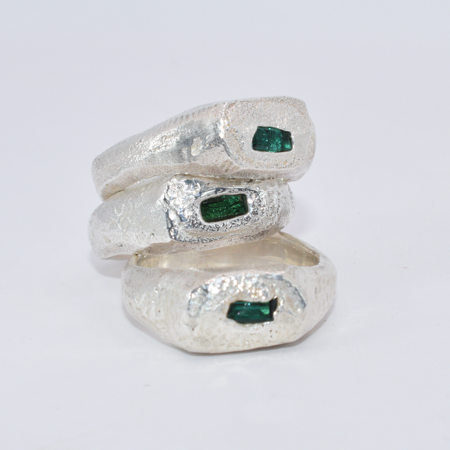 Three silver rings with embedded green gemstones on a white background