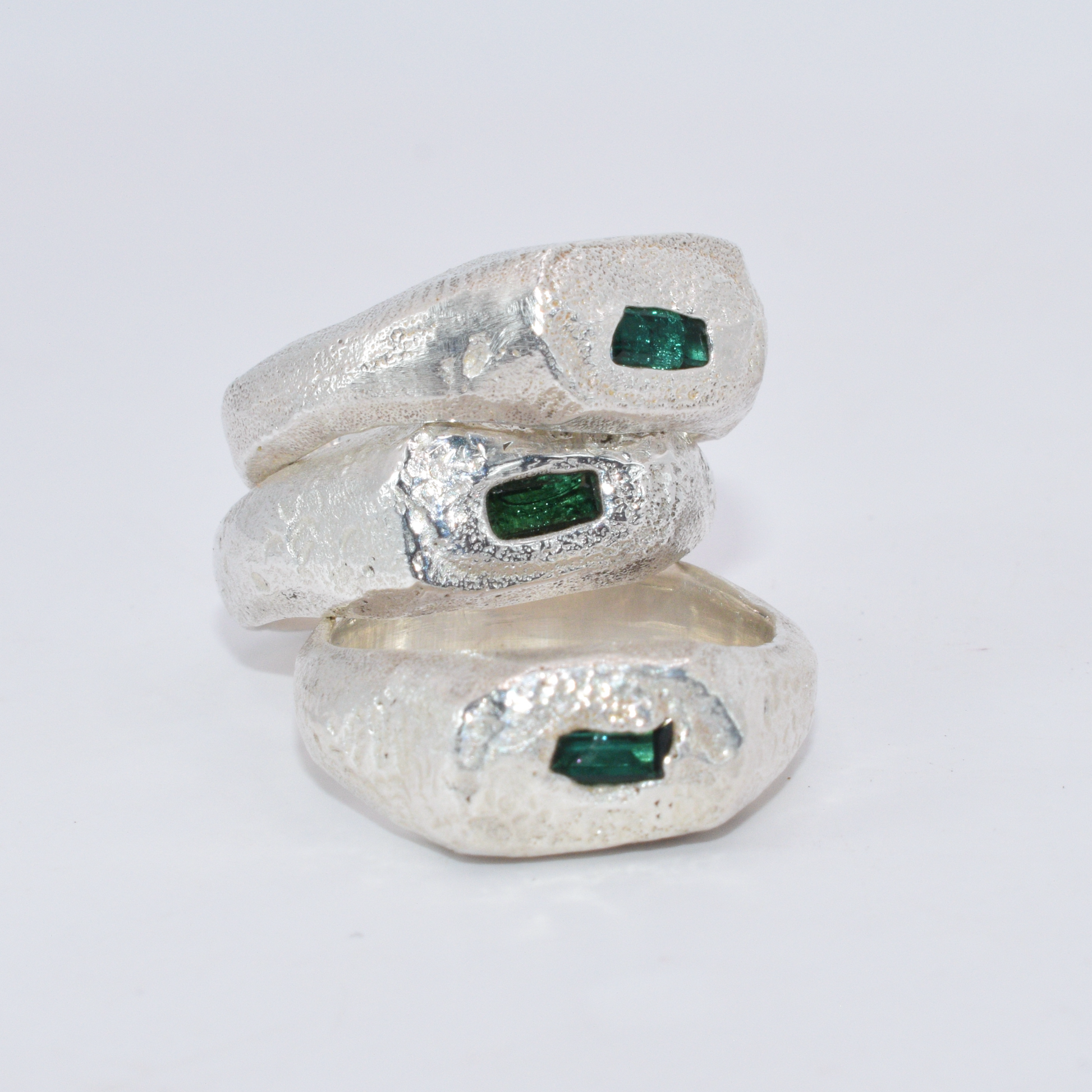 Three silver rings with embedded green gemstones on a white background