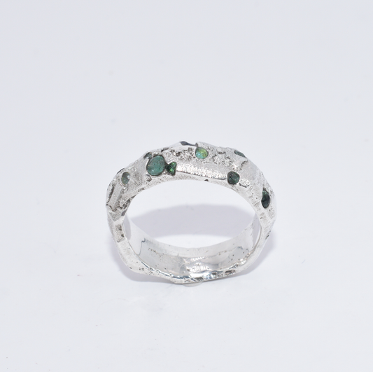 A silver ring with small emerald and synthetic sapphire stones set around its circumference.